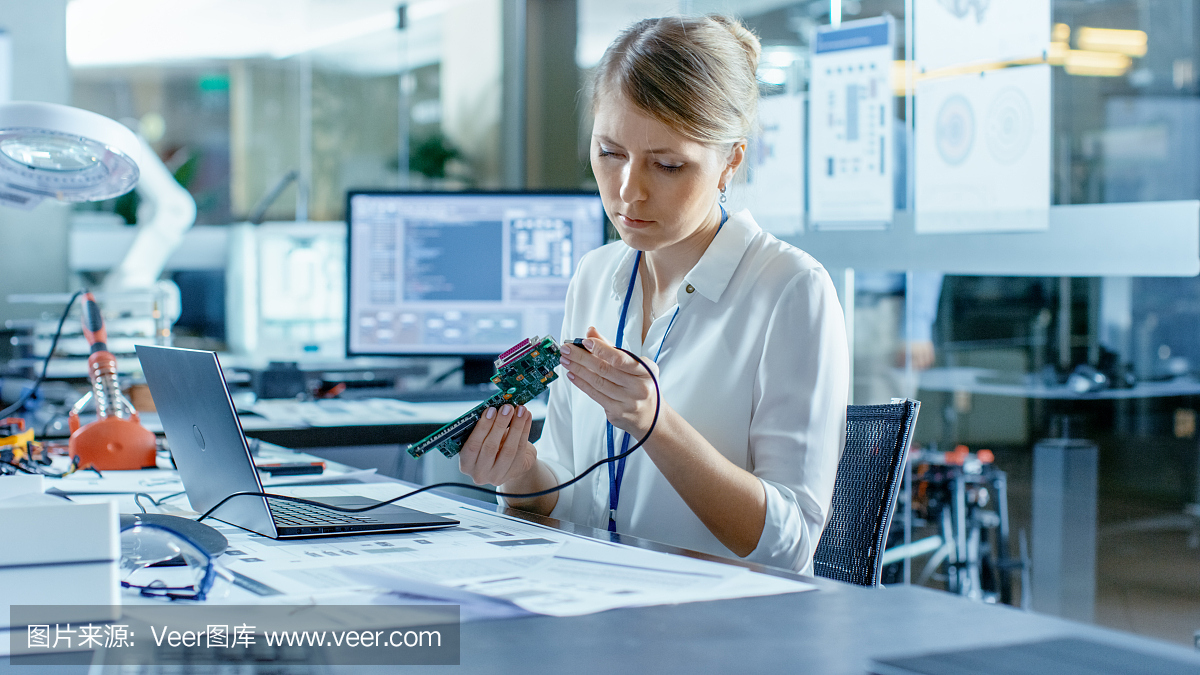 女計算機(jī)科學(xué)家將電路板連接到她的筆記本電腦并開始編程。她在先進(jìn)技術(shù)實驗室工作。